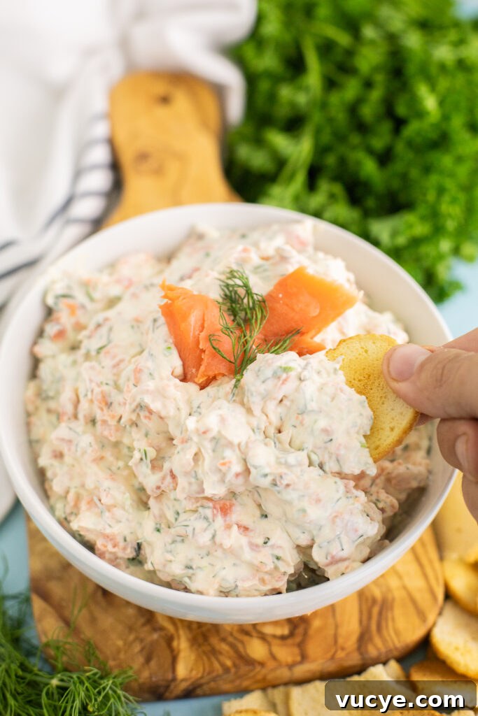 Salmon and Cream Cheese Dip & Spread: Lox-Style Appetizer Recipe 2 Smoked Salmon Dip in a white ceramic bowl topped with slices of smoked salmon and a sprig of fresh dill with a bagel chip dipping in.