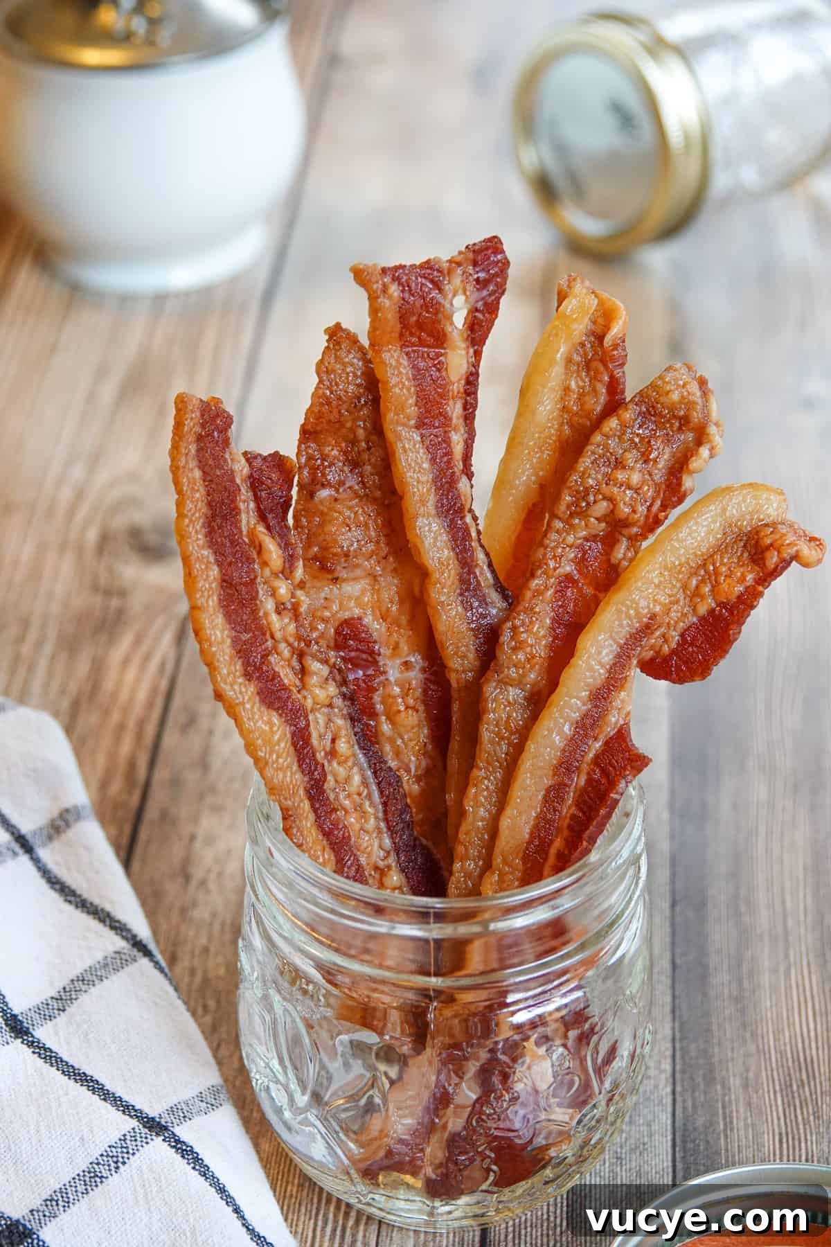 Bacon jerky in glass with towel, sugar cup, and mason jar in background
