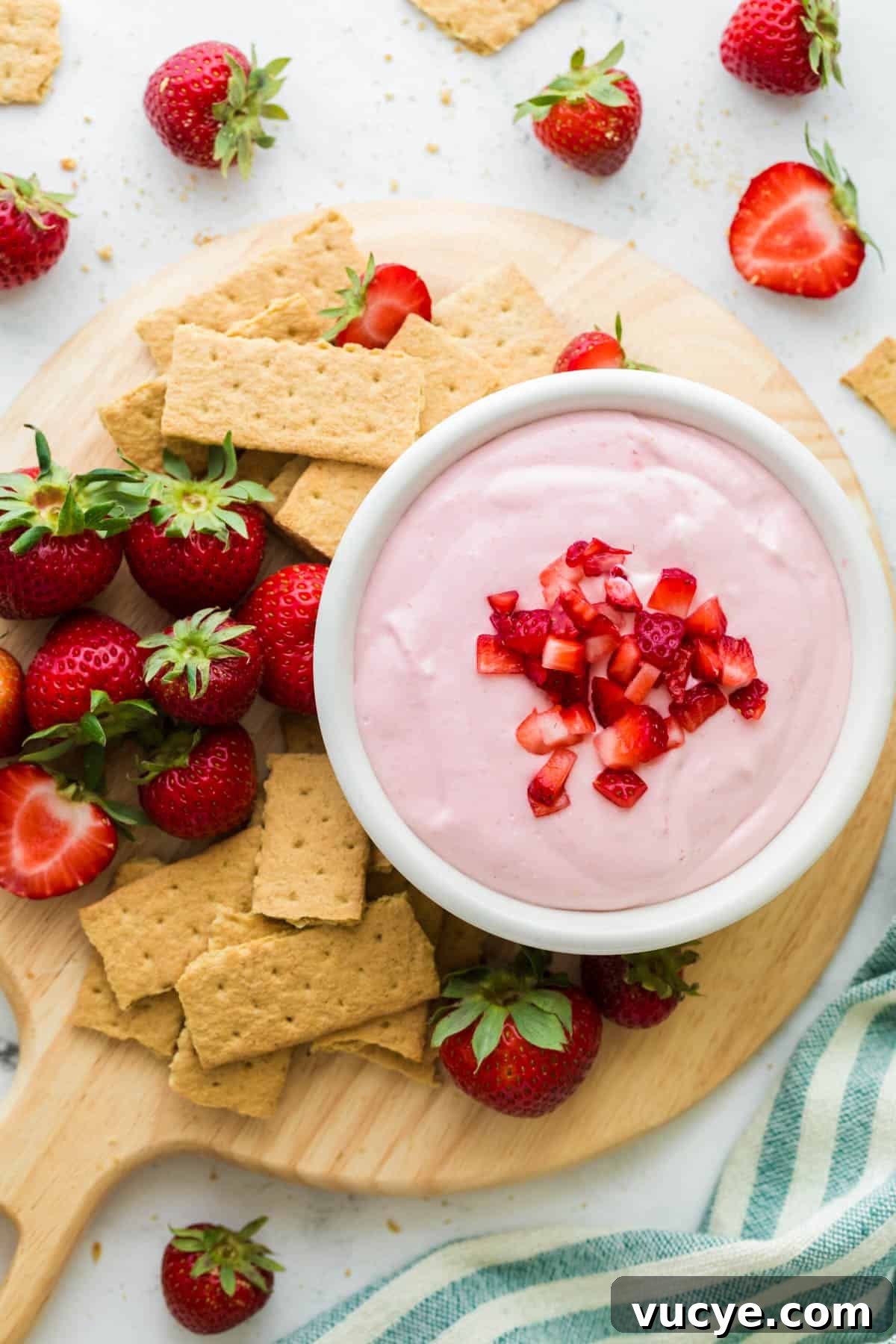 Creamy Strawberry Cheesecake Dip Recipe You’ll Love 2 Strawberry Cheesecake Dip in a white bowl on a wooden cutting board served with graham crackers and fresh strawberries.