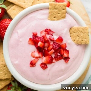 Two graham cracker pieces sit in a bowl of strawberry cream cheese dip.