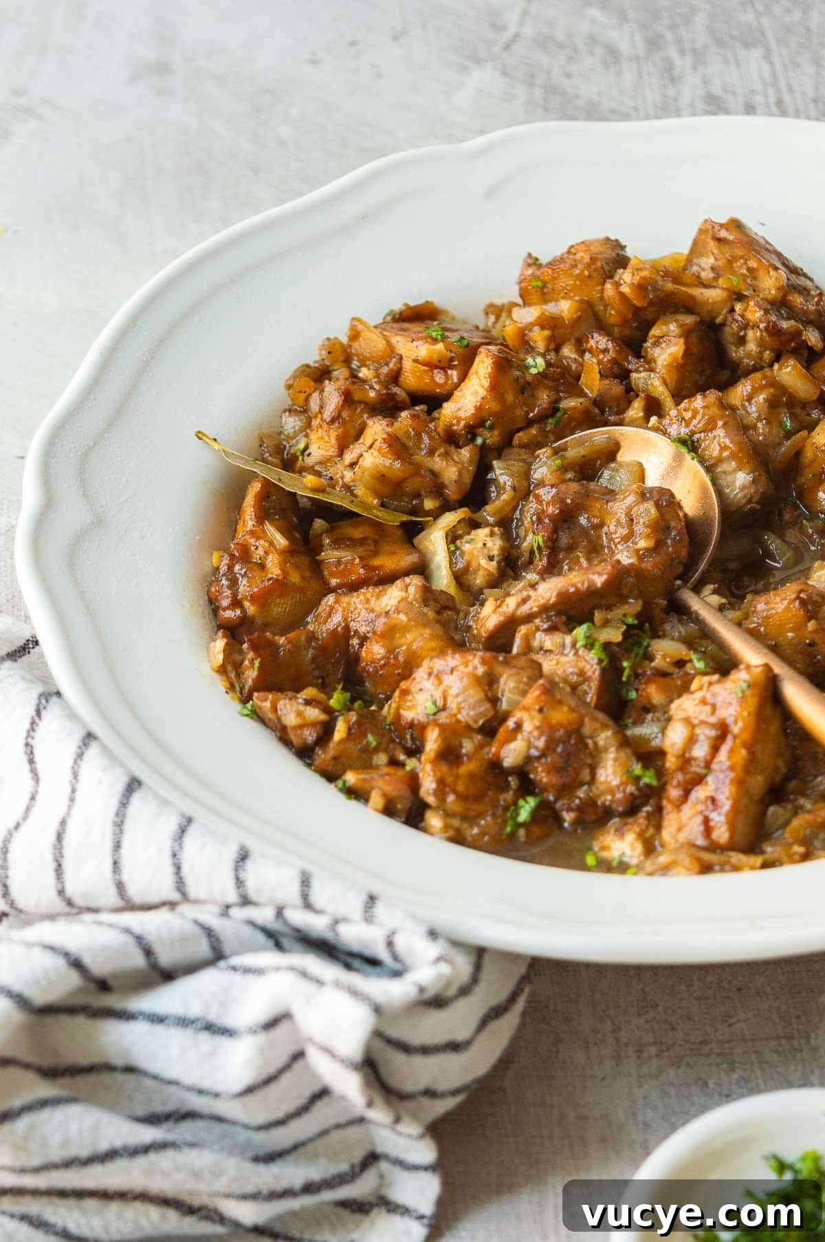 Vegan Tofu Adobo Recipe: Tangy Filipino-Style Comfort Food 10 A white plate on a black and white tea towel with chunky tofu and bay leaves in a brown sauce.