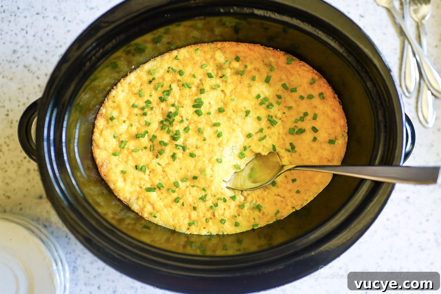 crock pot corn casserole in a slow cooker, with a spoon.