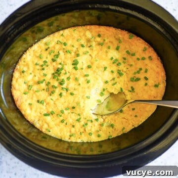 crock pot corn casserole in a slow cooker, with a spoon.