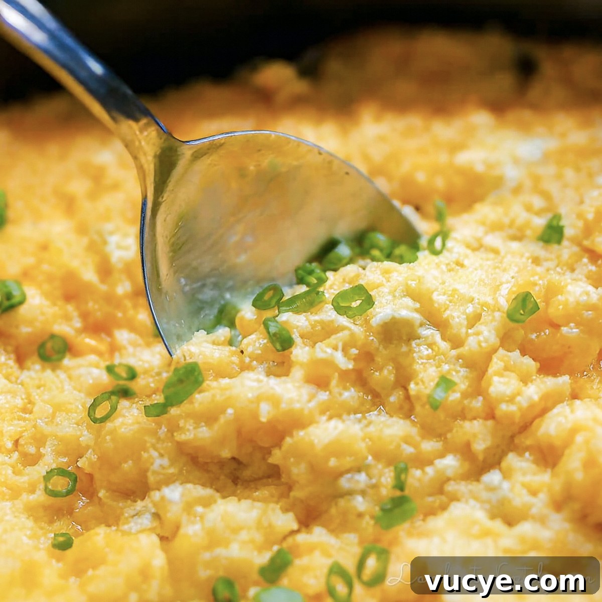 spoon in corn pudding, garnished with green onions.
