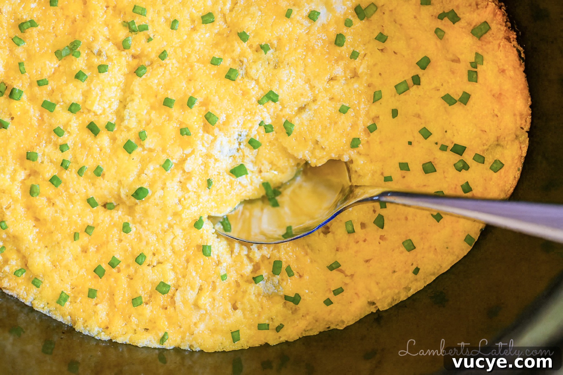 crock pot corn casserole in a slow cooker, with a spoon.