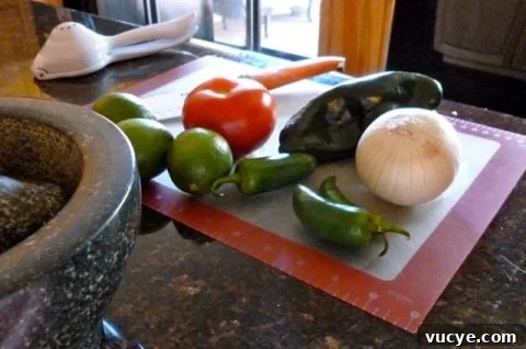 Fresh salsa ingredients including tomato, jalapeño, onion and lime on cutting mat.