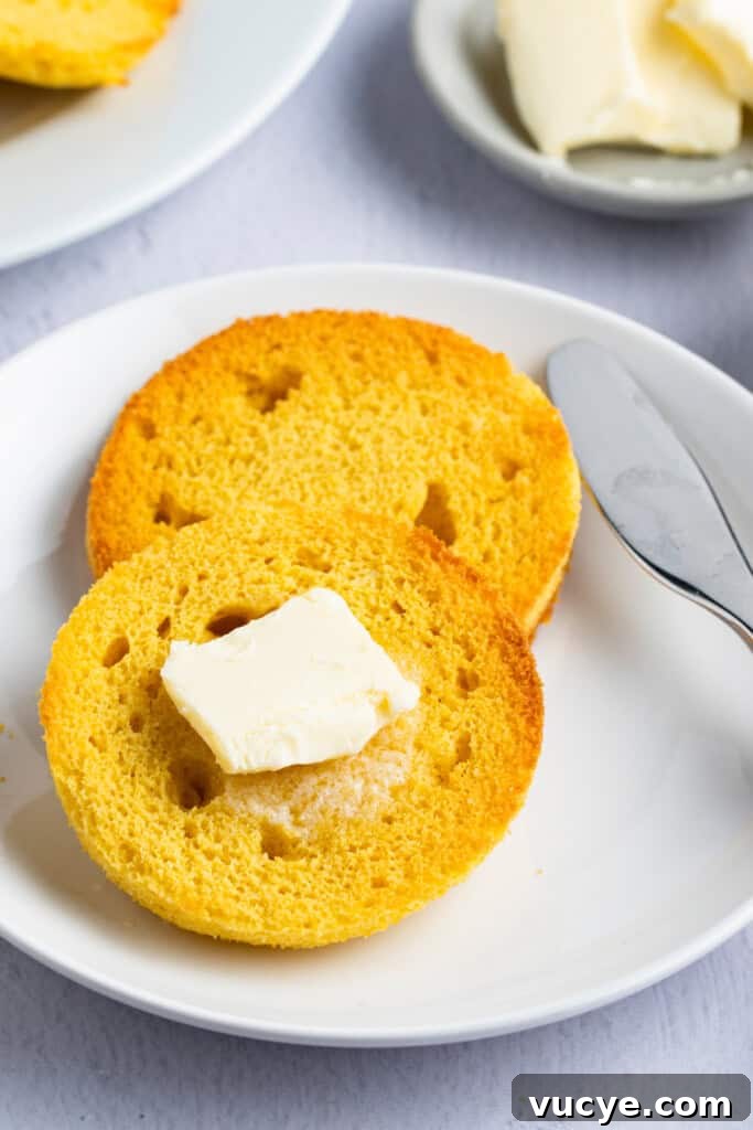 Keto English muffin, sliced in half, buttered, and set on a plate with a butter knife to the right.