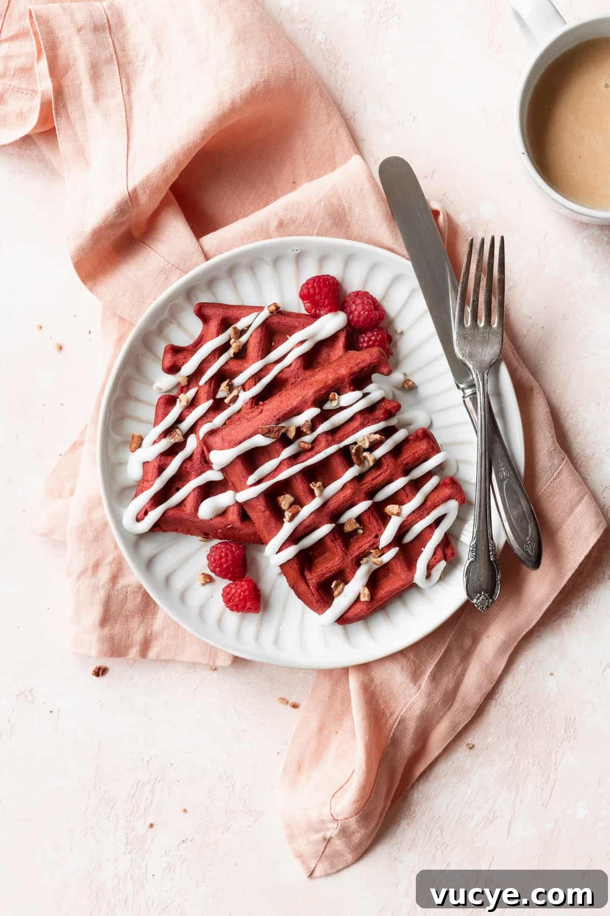 Red Velvet Waffles Recipe: fluffy, rich, and irresistible 2 An overhead shot of a white plate of red velvet waffles with cream cheese drizzle and pecans.
