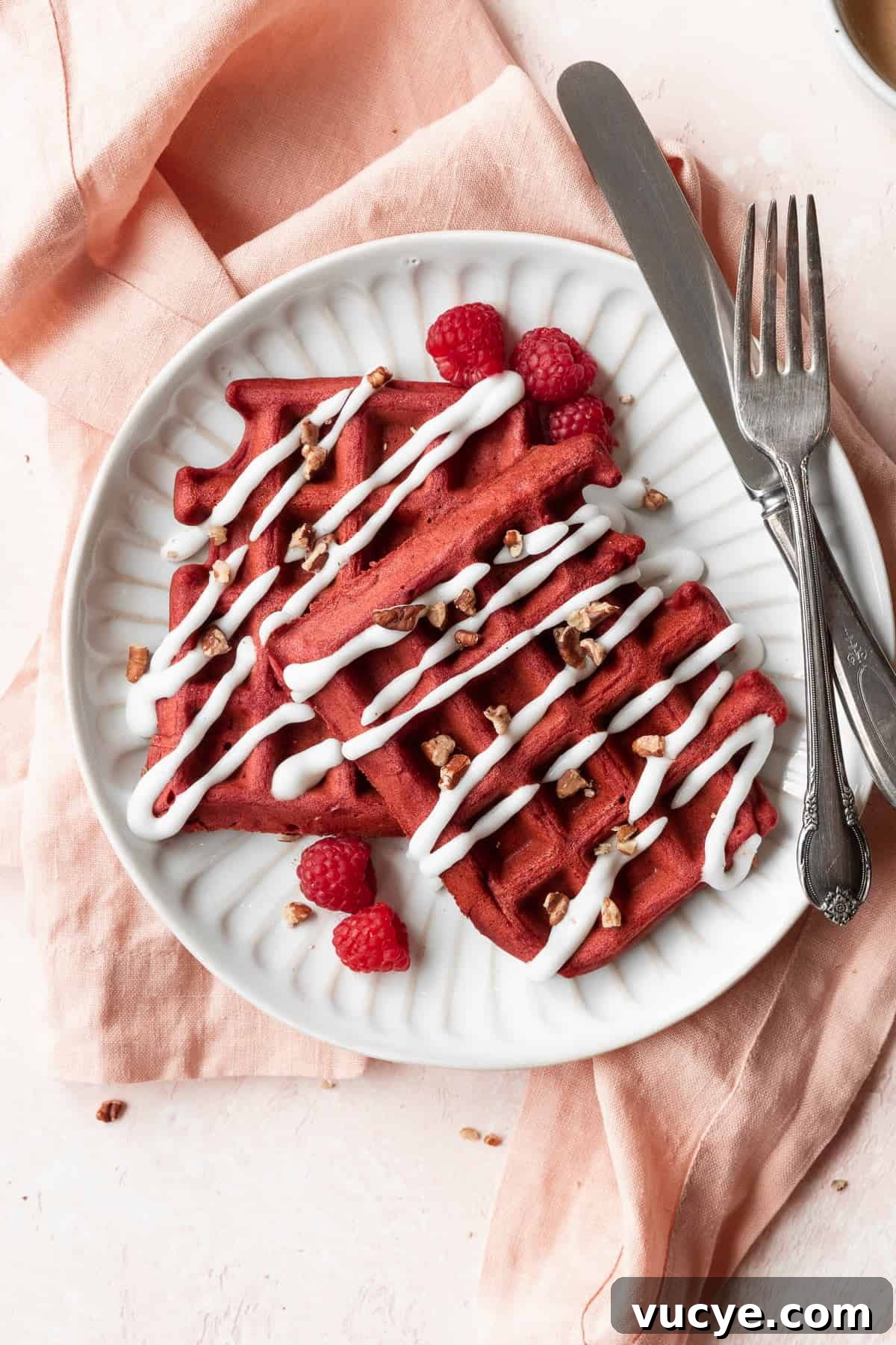Red Velvet Waffles Recipe: fluffy, rich, and irresistible 13 A closeup shot of a white plate of red velvet waffles with cream cheese glaze and raspberries.