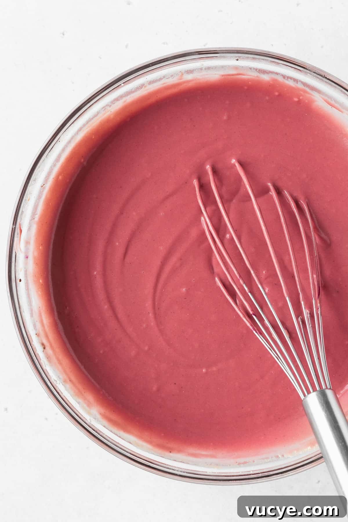 Red Velvet Waffles Recipe: fluffy, rich, and irresistible 6 A closeup overhead shot of a glass mixing bowl of red velvet waffle batter with a whisk.