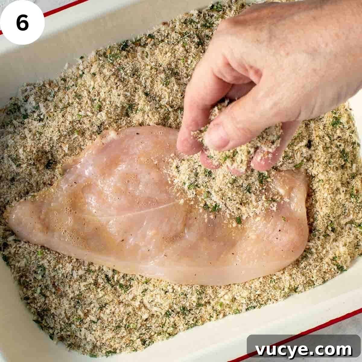 Covering chicken breast with breadcrumbs.