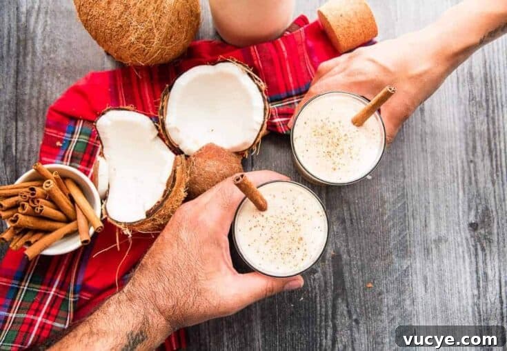Overhead view of hands holding a couple coquito cocktails garnished with cinnamon.