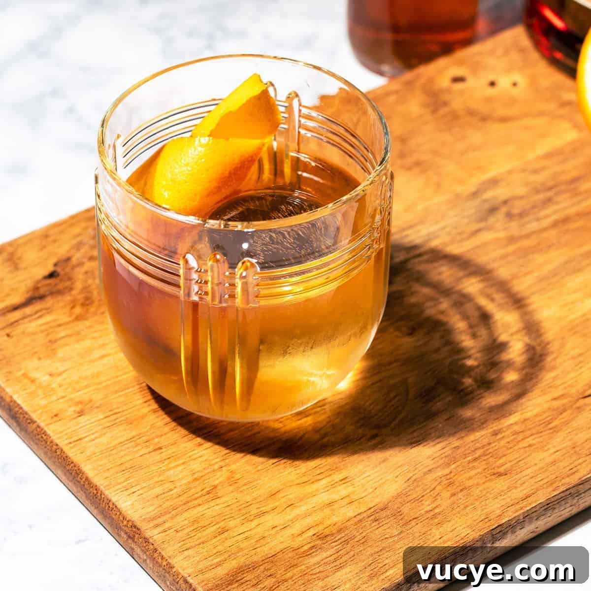 A rum old fashioned cocktail garnished with an orange peel twist.