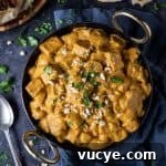 Vegan mushroom and tofu korma in a black karahi pan on a dark background with chopped cahews, coriander and naan breads.