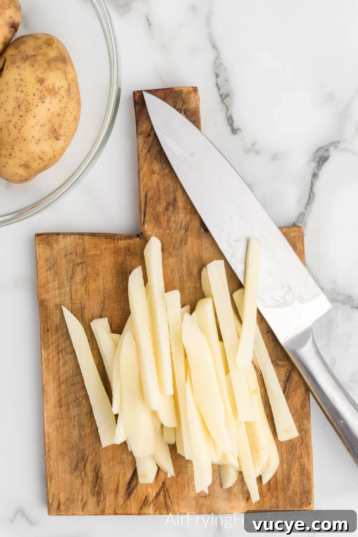Crispy Air Fryer Truffle Fries Recipe 4 Potatoes sliced into fries with a knife on a cutting board.