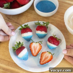 Red, White & Blue Dipped Strawberries for 4th of July 7 A plate of strawberries dipped in white chocolate and blue sugar sits on a wooden surface. Two hands hold the plate. A bowl of plain strawberries, a bowl of blue sugar, and a bowl of white chocolate are nearby.
