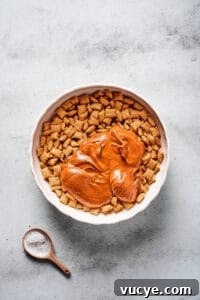 Crunchy Peanut Butter Muddy Buddies Recipe 4 A large mixing bowl of Chex cereal, with a melted peanut butter chocolate mixture poured on top.