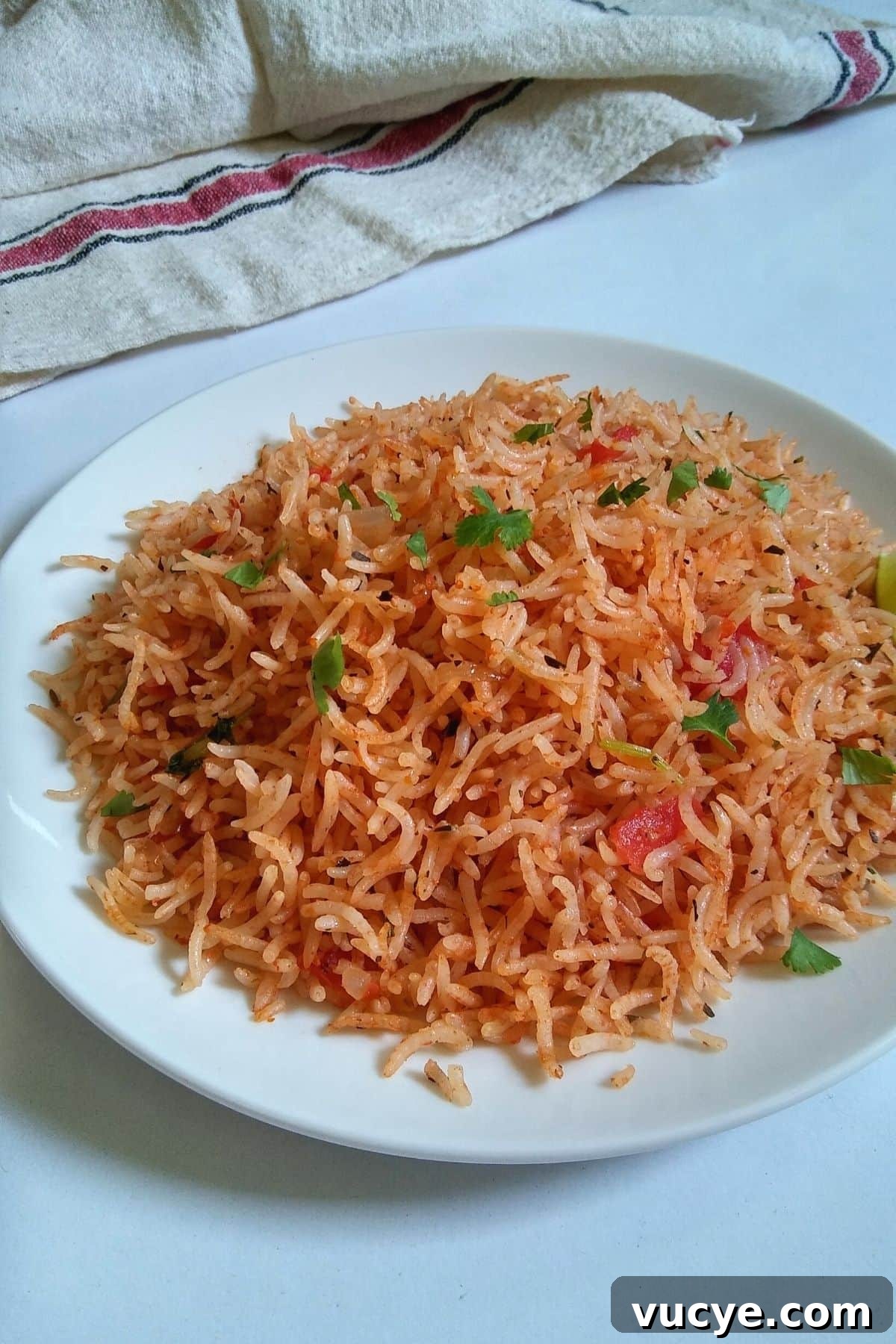 Image: Vibrant orangish red rice served on a white plate along with two lime wedges.