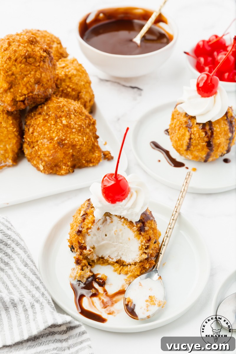 Homemade Fried Ice Cream Recipe: Crispy Shell & Creamy Center 6 a table set with two servings of fried ice cream, one has been partially eaten. In the background is a bowl of chocolate syrup and a bowl of cherries