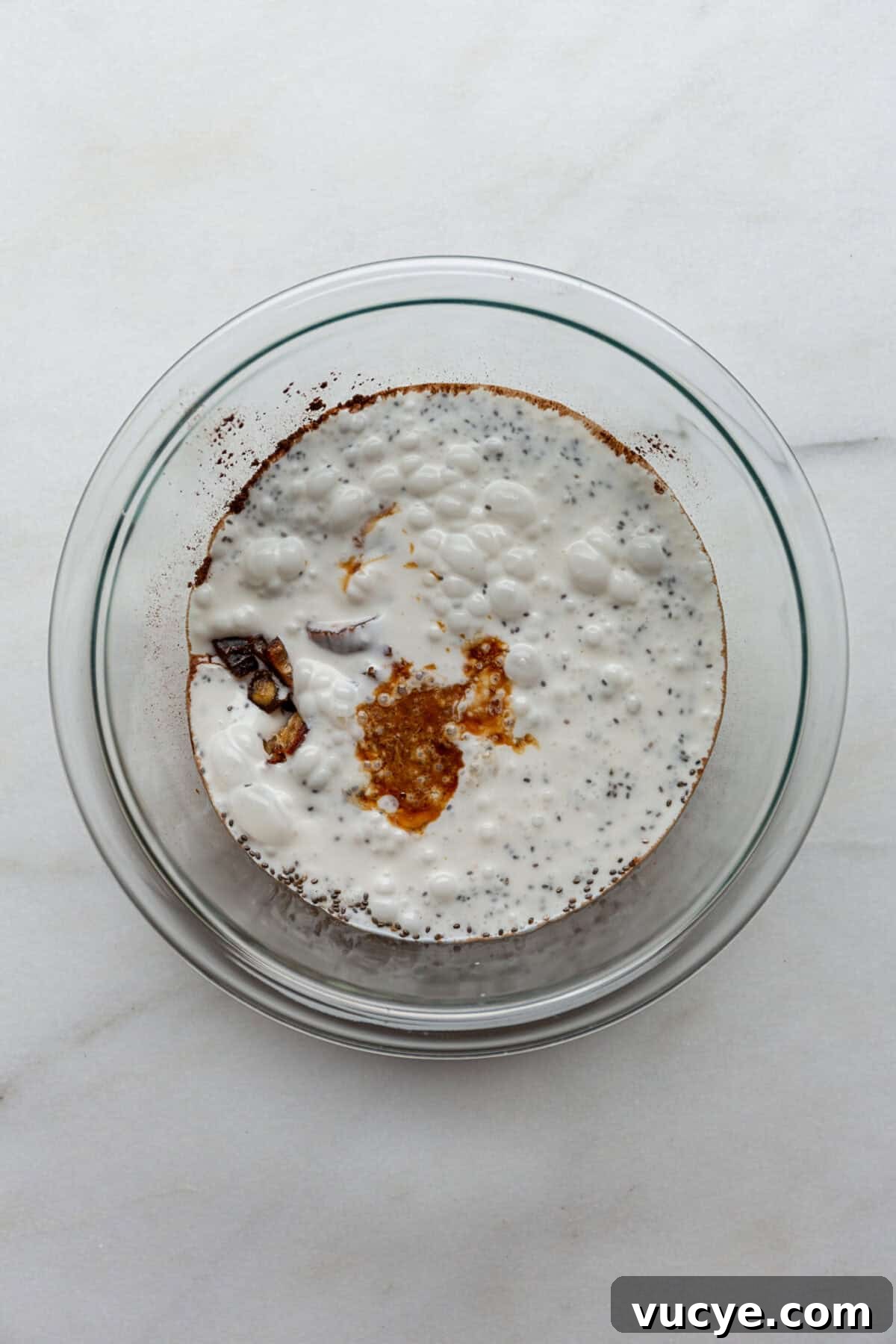 Snickers-Inspired Chia Pudding Recipe: Chocolate Peanut Butter Parfait 5 coconut milk, vanilla, chia seeds, dates and cocoa powder in a clear mixing bowl.