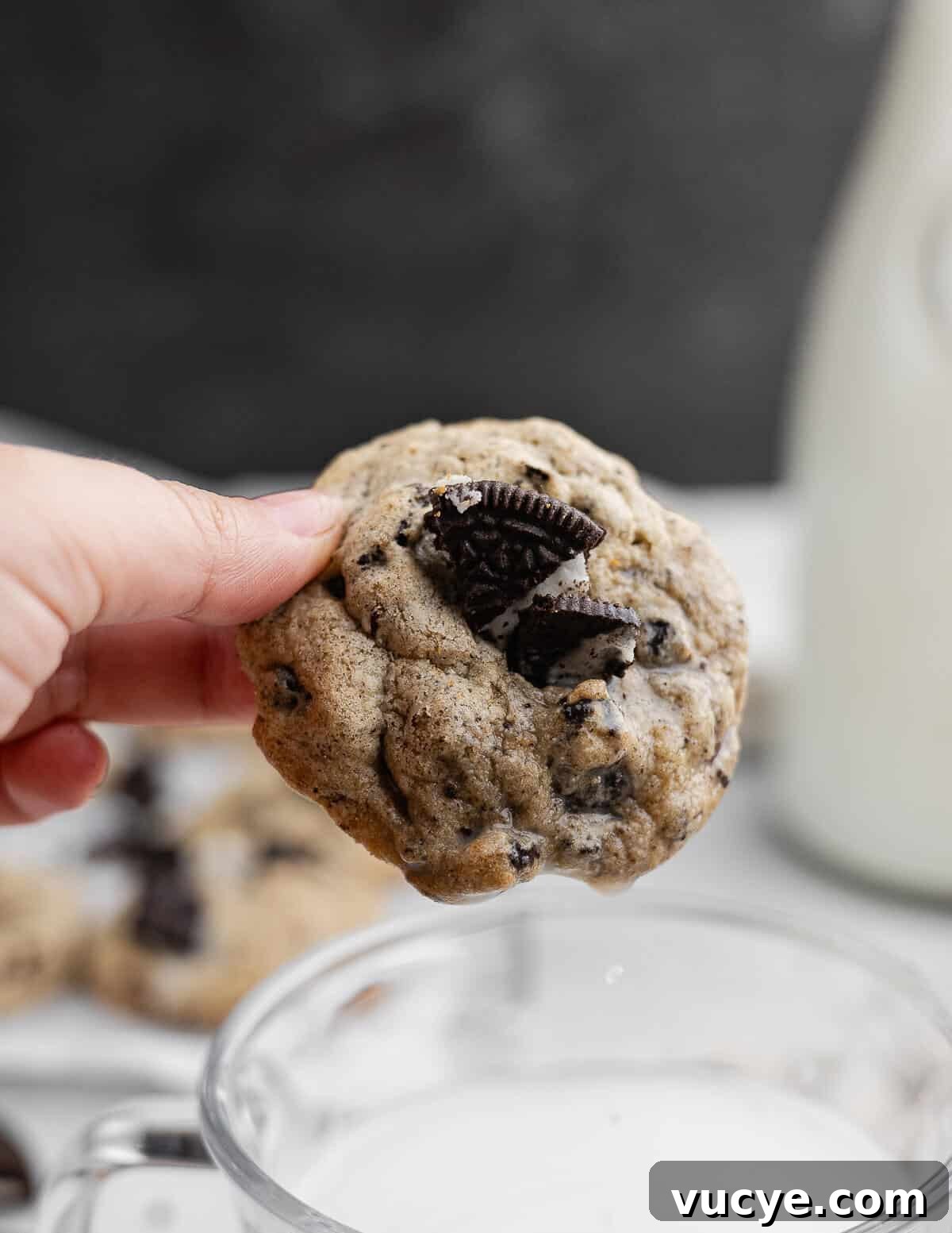 Oreo Chocolate Chip Cookies Recipe — Crispy Edges, Chewy Center 2 hand holding an Oreo chocolate chip cookie above a glass of milk.