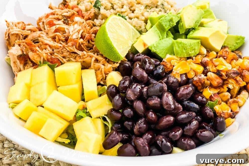 Bowl filled with shredded salsa chicken, quinoa, black beans, roasted corn, diced mango, and diced avocado garnished with a wedge of lime and fresh cilantro