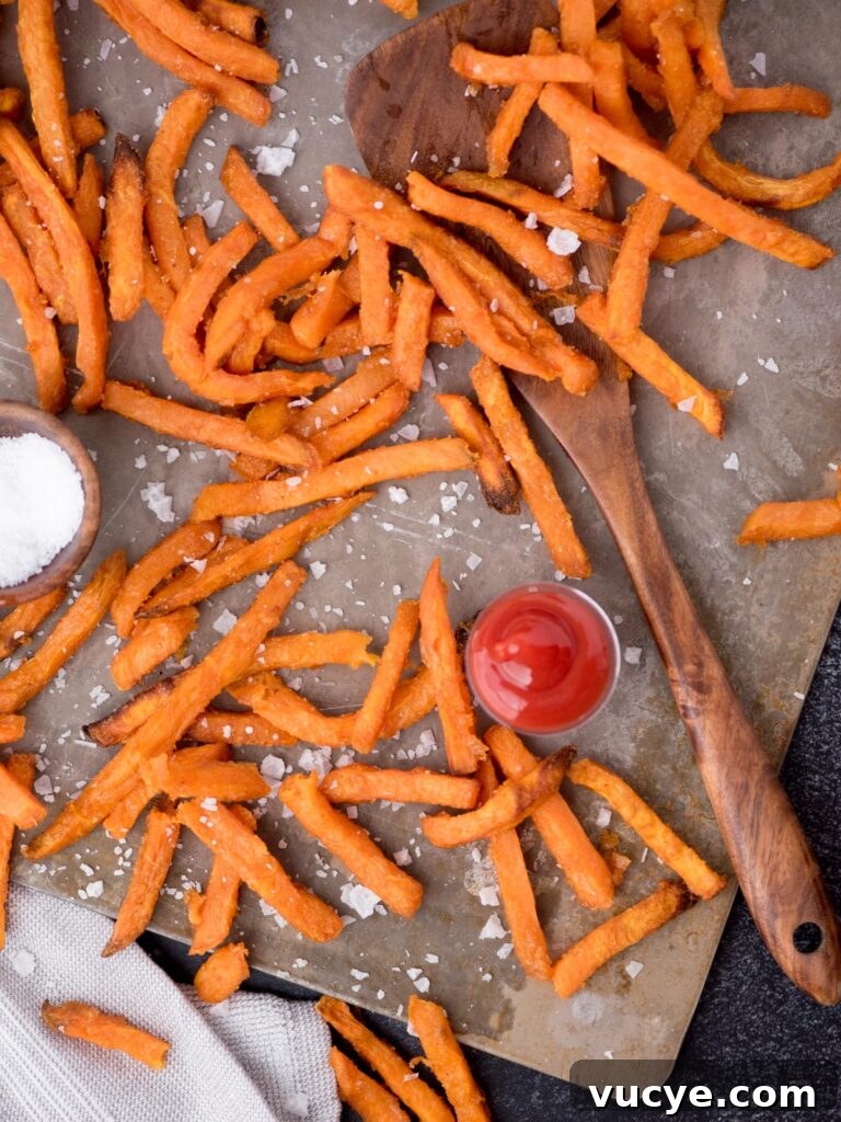 Crispy Air Fryer Sweet Potato Fries from Frozen 2 Wooden spoon laying amongst sweet potato french fries on a baking sheet and sea salt sprinkled over the top.