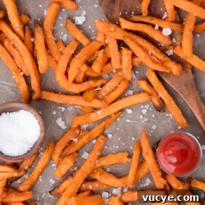 Crispy Air Fryer Sweet Potato Fries from Frozen 8 Sea salt sprinkled over sweet potato fries on parchment paper with a small dish of ketchup and sea salt by them.