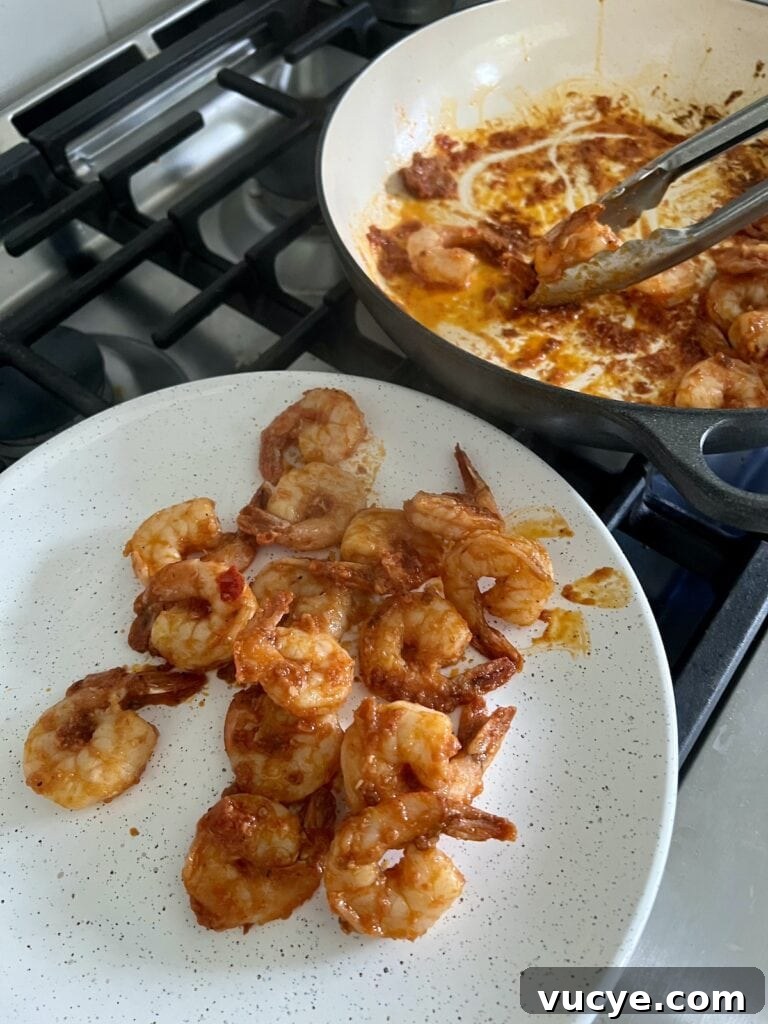 Transferring spicy tomato shrimp from pan to white plate with tongs