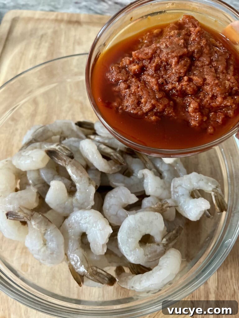 Pouring spicy tomato marinade into bowl of raw shrimp.