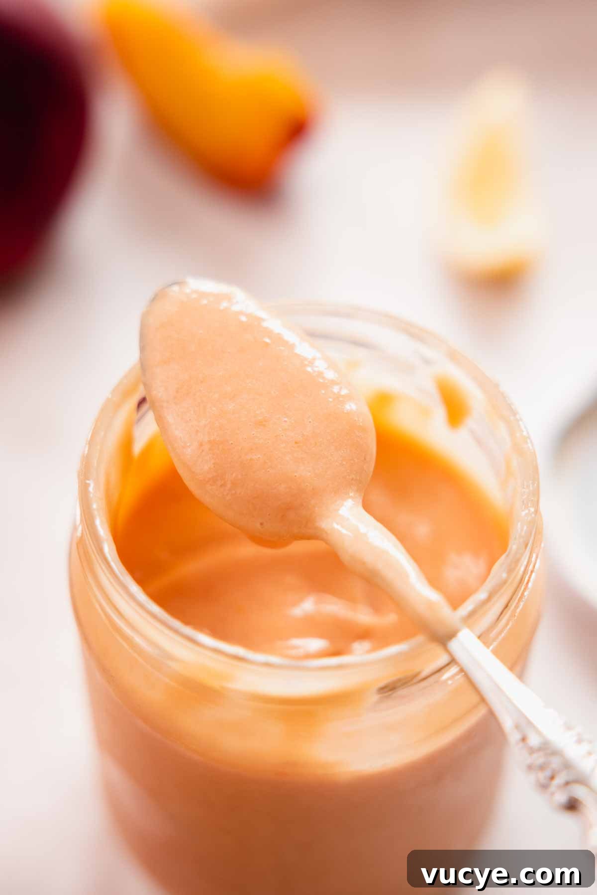 Silky Homemade Peach Curd Recipe for Tarts & Toast 3 close up of curd dripping of a spoon sitting on top of a jar