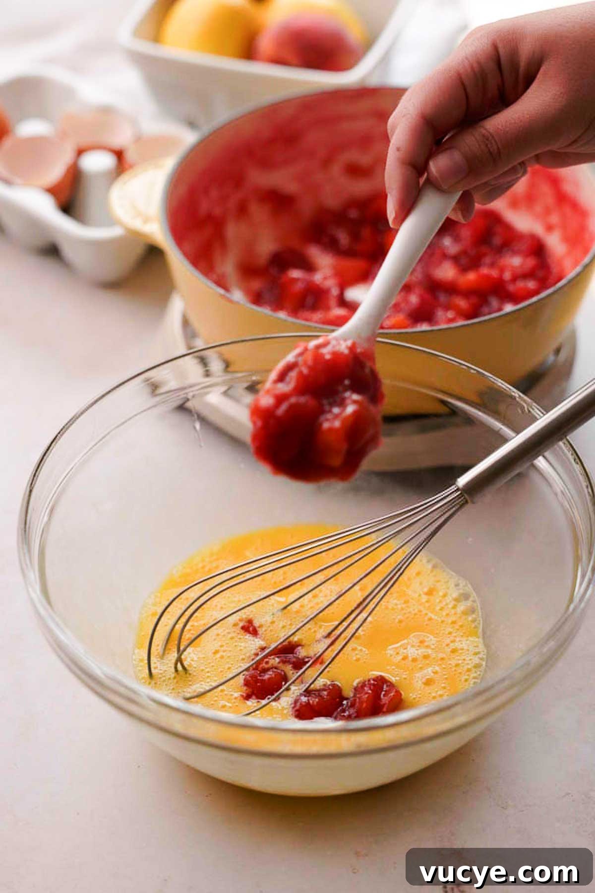 Silky Homemade Peach Curd Recipe for Tarts & Toast 10 adding spoonfuls of hot peach mixture into egg mixture in a bowl