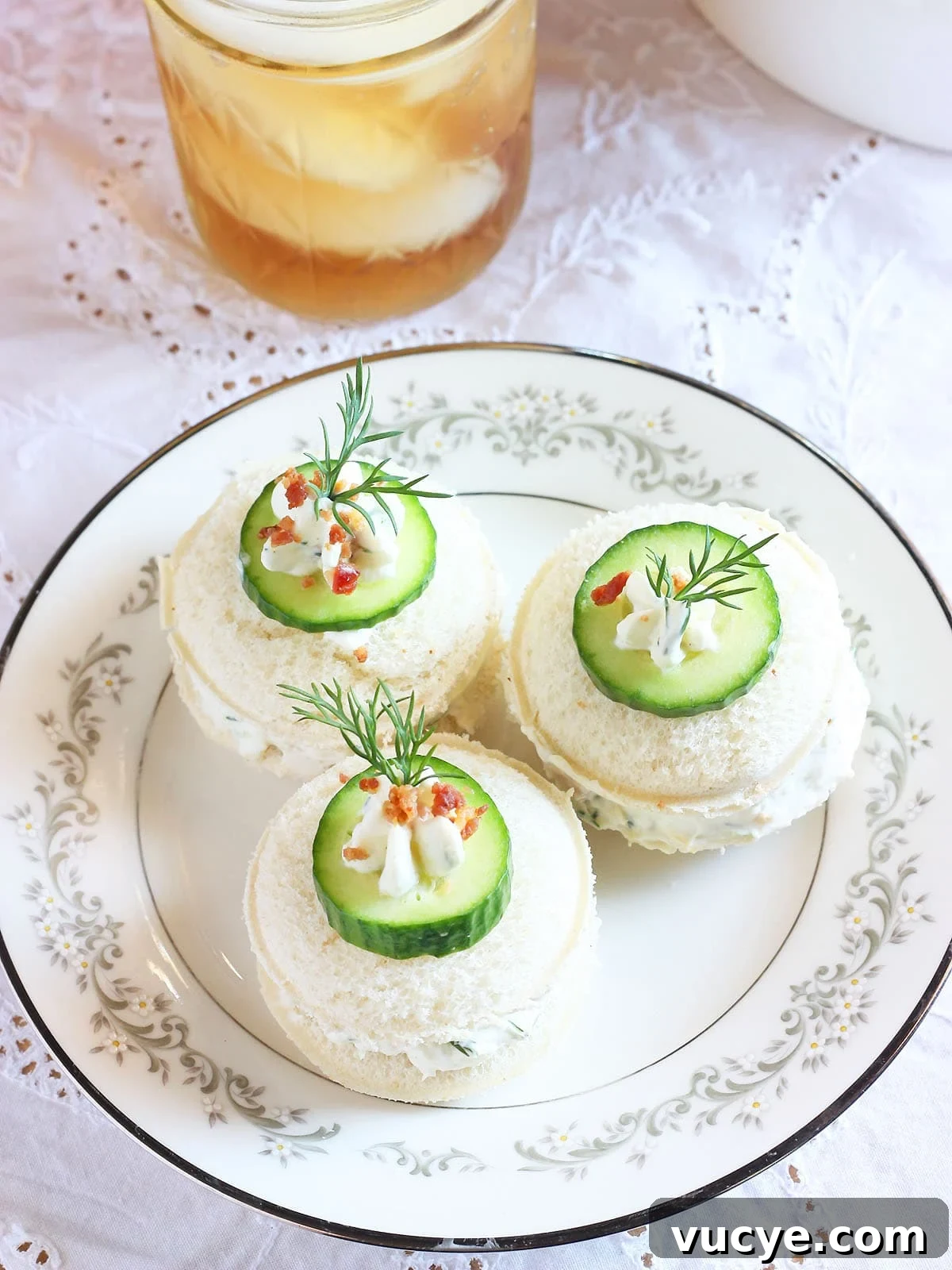 Cucumber Tea Sandwich Recipe for Light, Refreshing Tea Parties 9 Three cucumber tea sandwiches garnished with a dollop of cream cheese, cucumber slice, fresh dill and bacon bits. Glass of iced tea in the background.