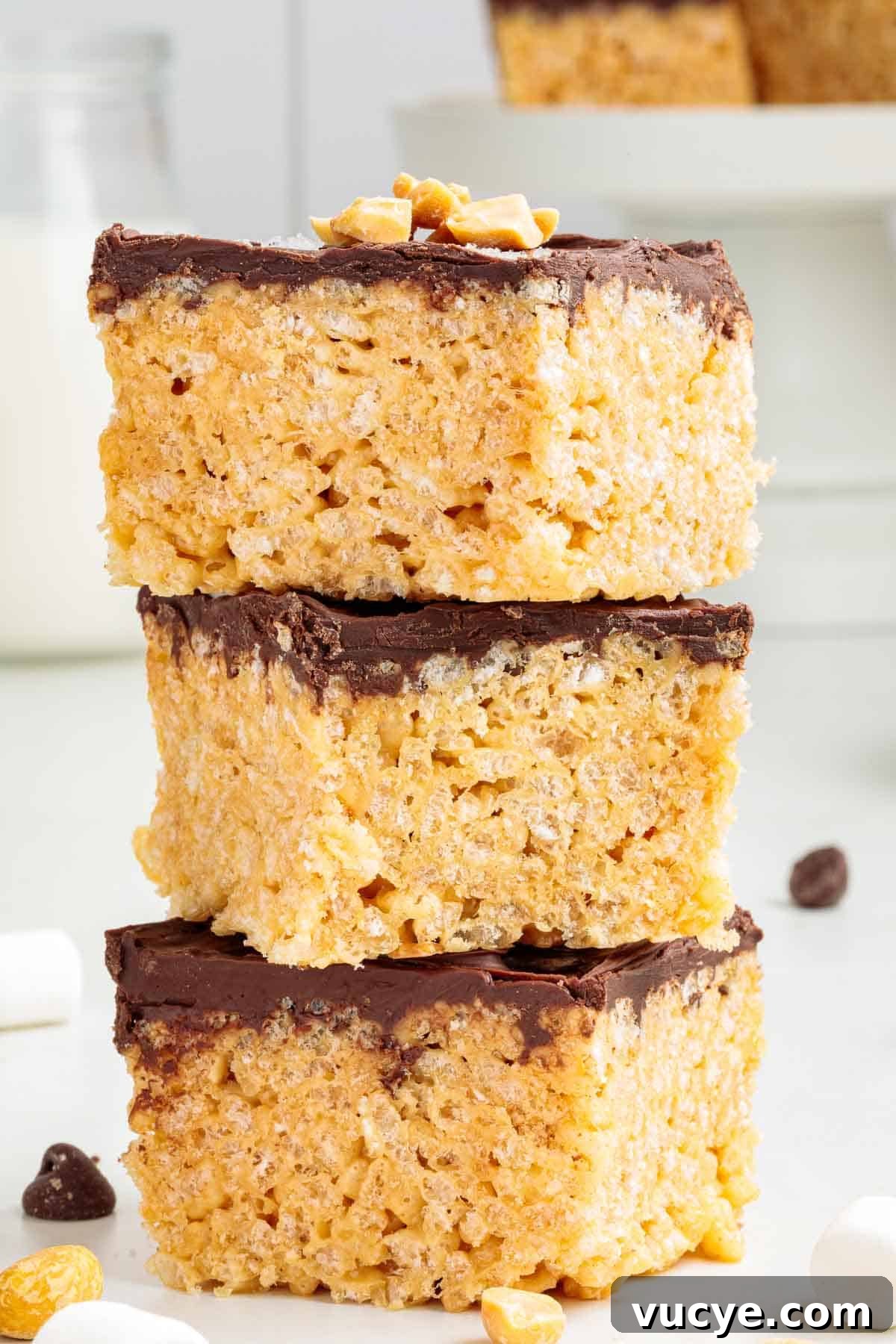 A stack of three thick chocolate-covered Rice Krispie treats with visible crispy cereal texture and chopped peanuts on top.