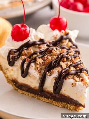 Slice of banana split pie topped with whipped cream, chopped pecans, chocolate syrup, and cherries.