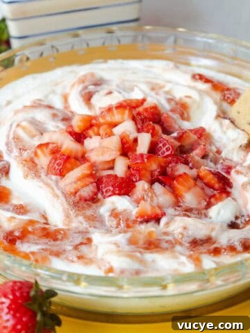Strawberry cheesecake dip topped with swirled strawberry jam and diced fresh strawberries served in a glass pie dish.
