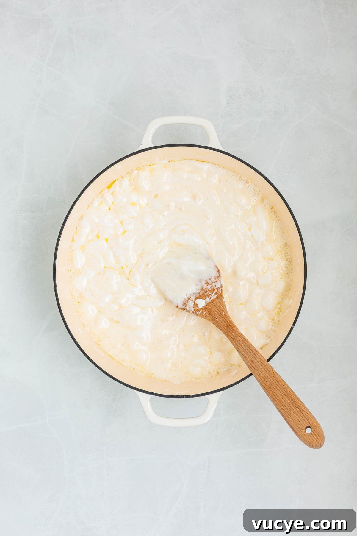 A pot filled with melted marshmallows and butter being stirred with a wooden spatula, forming the gooey base of the Rice Krispie treat mixture.