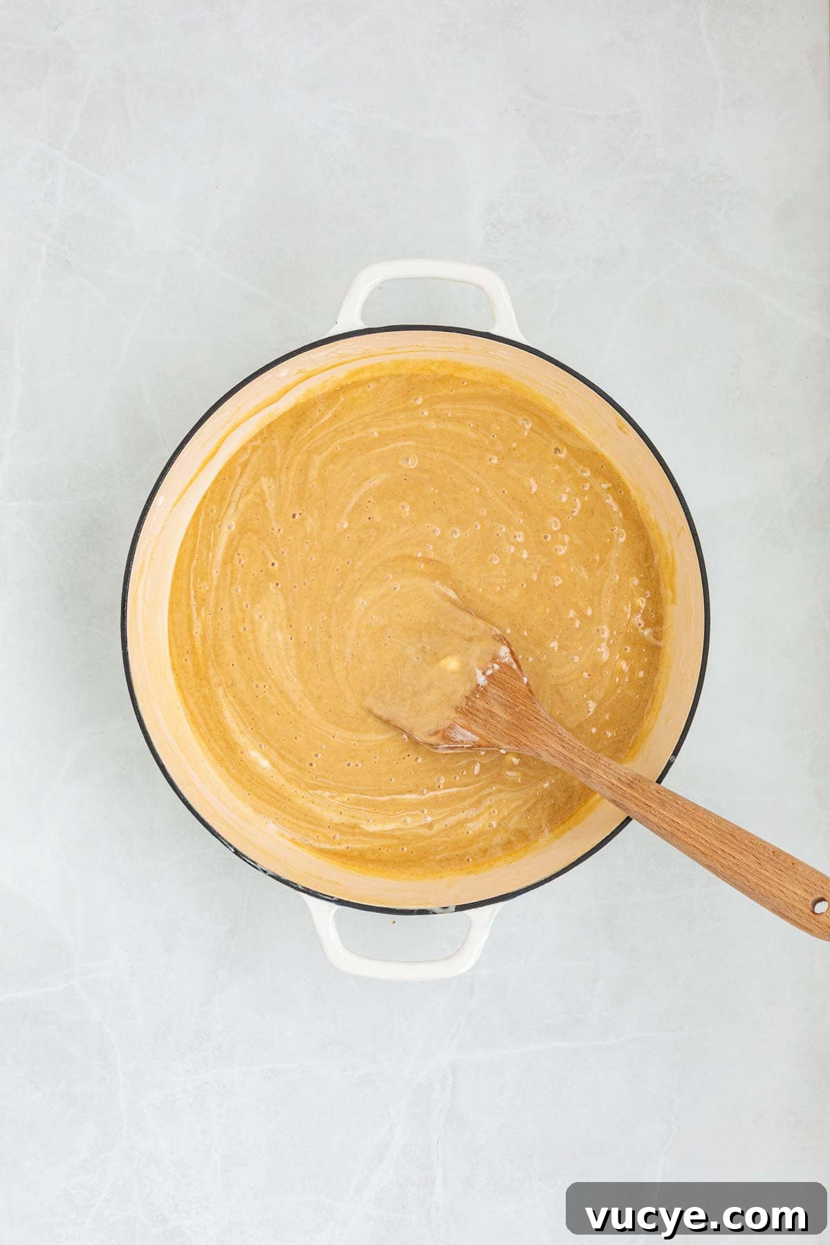 Creamy peanut butter mixed into the melted marshmallow mixture inside a pot, stirred with a wooden spatula.