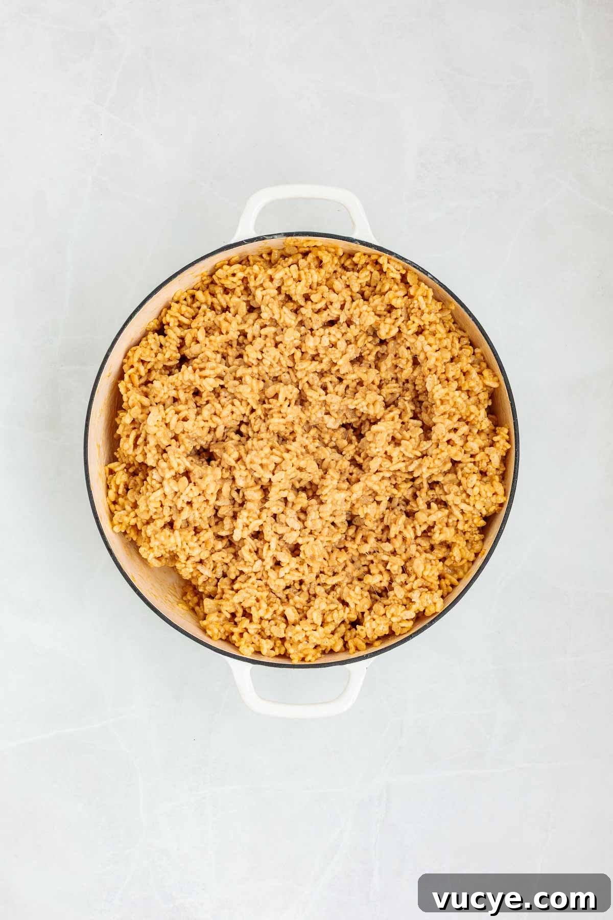 Crispy rice cereal fully mixed into the melted peanut butter-marshmallow base, forming a thick and sticky mixture in a large pot.
