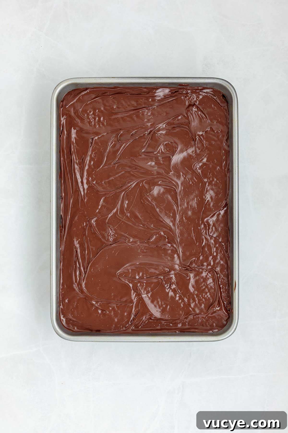Top view of a baking tray with a smooth layer of melted chocolate spread over the Rice Krispie treat base.