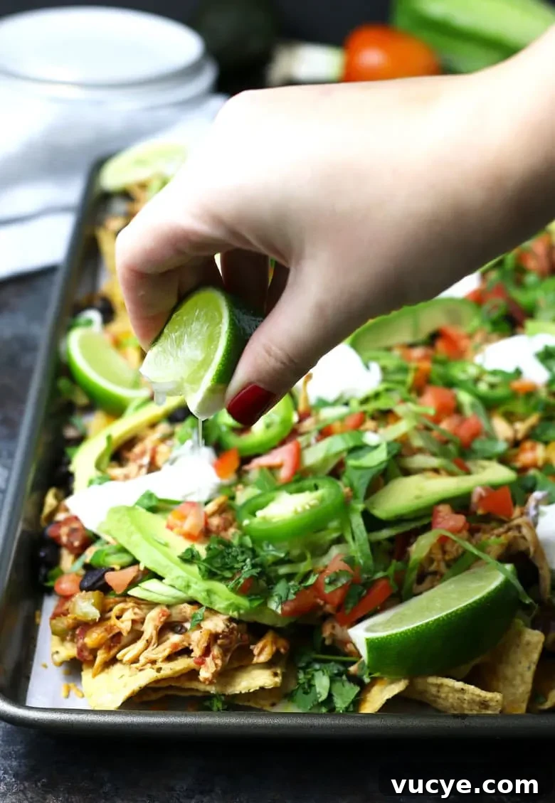 Sheet Pan Chicken Nachos with Loaded Toppings 6 squeezing lime juice on chicken nachos