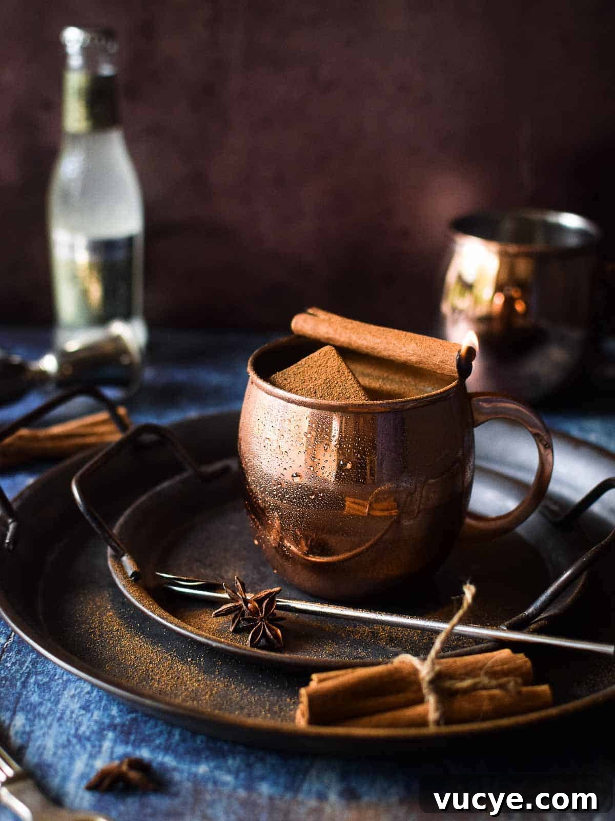 Chai Moscow mule in a copper mug with a cinnamon stick on fire.