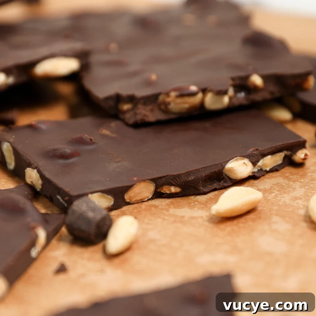 Chocolate Bark with Honey Glazed Almonds, broken into pieces and arranged on a brown surface, features whole almonds embedded in rich dark chocolate, with extra glazed almonds scattered around.