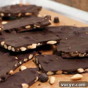 Broken pieces of chocolate bark with honey glazed almonds and whole nuts scattered on a brown surface.