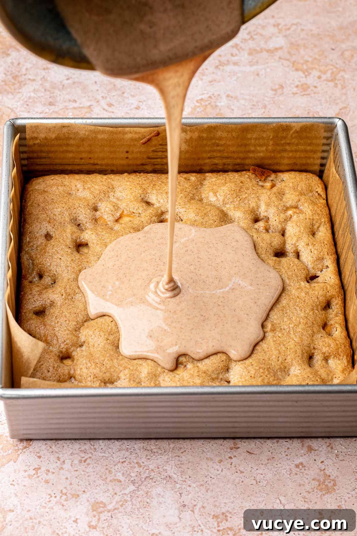Apple Cinnamon Blondie Recipe — Chewy Spiced Apple Bars 9 Cinnamon icing being drizzled onto baked cinnamon apple blondies in a pan.