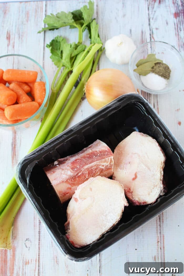 Ingredients for bone broth: celery, carrots, garlic, and onion lay next to beef bones on a tray. A bowl of spices with bay leaves completes the setup. Perfectly suited for a slow cooker, these elements promise depth and warmth in every sip.