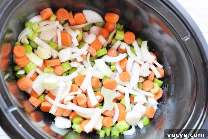 Chopped carrots, celery, onions, and potatoes simmer in a savory broth recipe within the slow cooker.