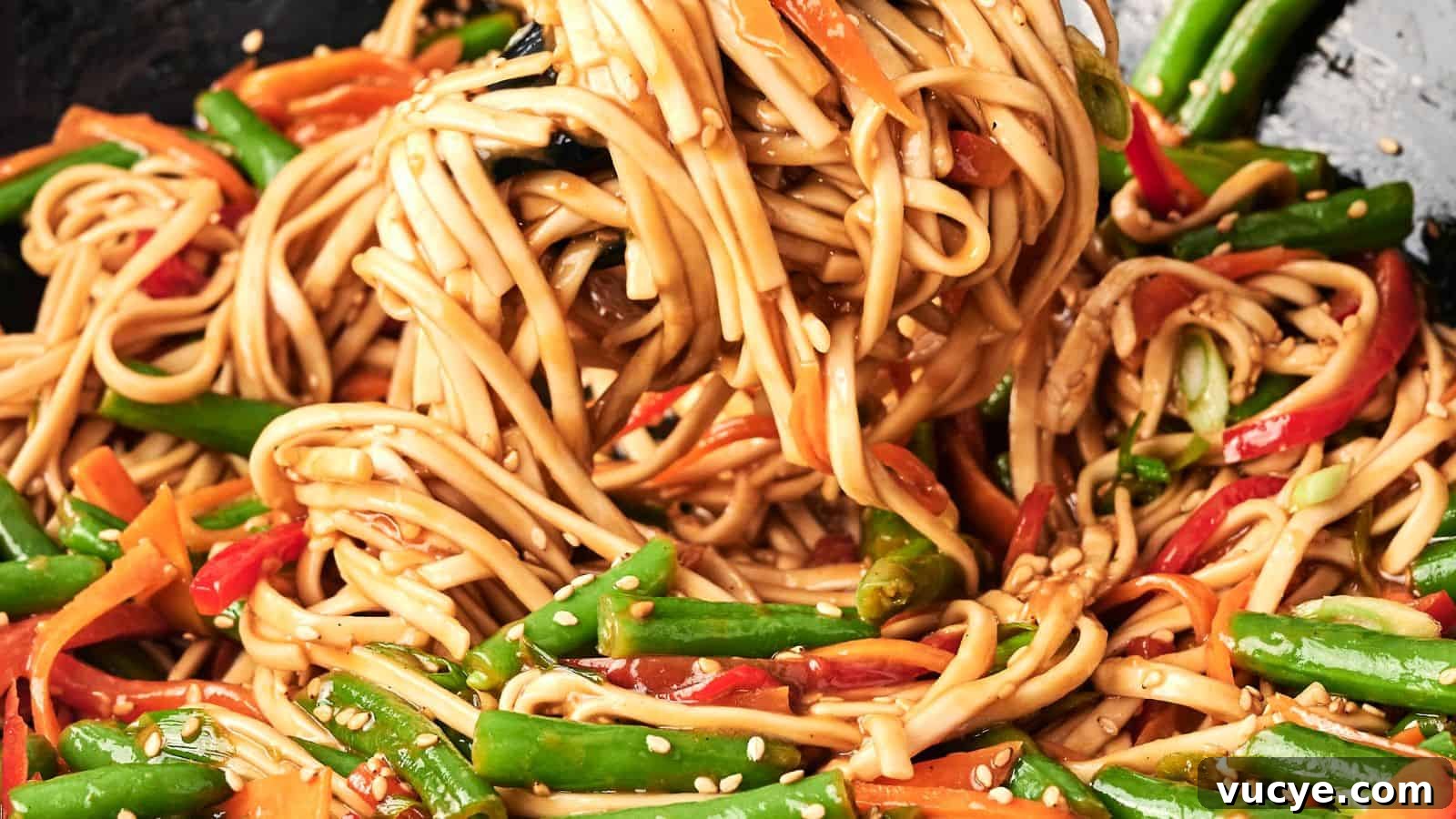 A close-up of stir-fried noodles with green beans, red bell peppers, and carrots, garnished with sesame seeds.