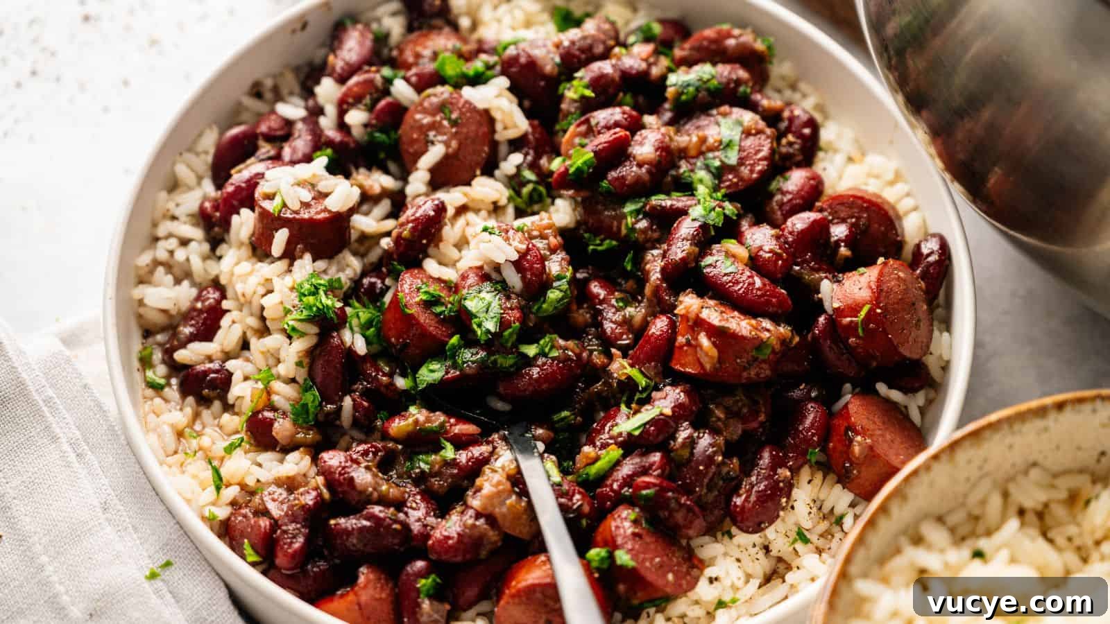A bowl of white rice topped with kidney beans, sliced sausage, and chopped herbs, with a fork resting inside.