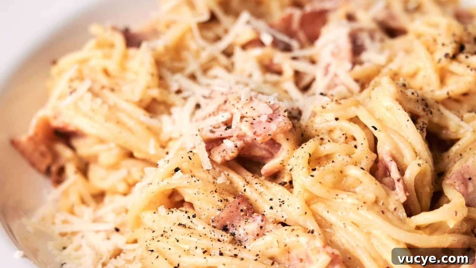 A close-up image of spaghetti carbonara topped with grated cheese and freshly ground black pepper.